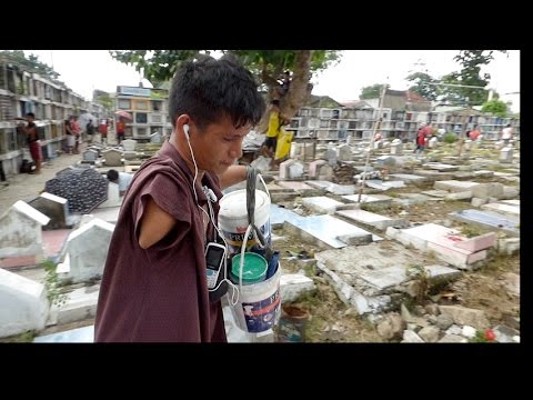 ALL SOULS DAY. NO ARMS.  PAINTS (LETTERING) TOMBSTONES WITH FEET. CEBU PHILIPPINES.